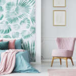 Comfortable pale pink upholstered chair in a cozy bedroom interior with double bed and green and leaves decorations